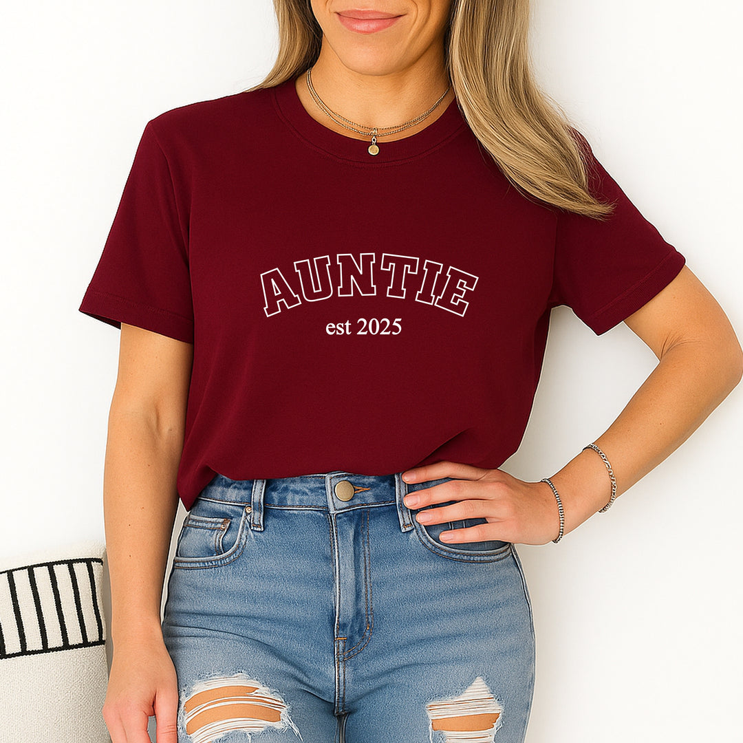 Person wearing a maroon t-shirt with 'AUNTIE est 2025' text, standing against a white background.