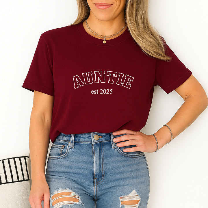 Person wearing a maroon t-shirt with 'AUNTIE est 2025' text, standing against a white background.