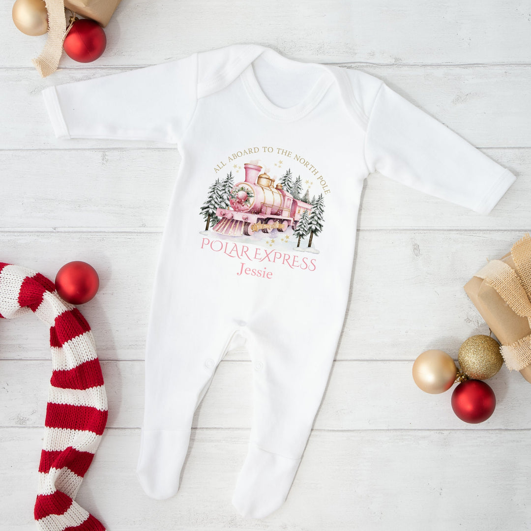 White baby onesie with 'Polar Express' design on a light wooden surface with Christmas decor.