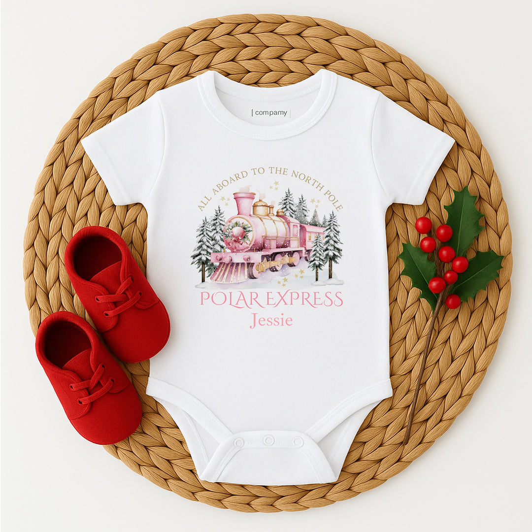 White baby onesie with Polar Express design and red shoes on a woven mat.