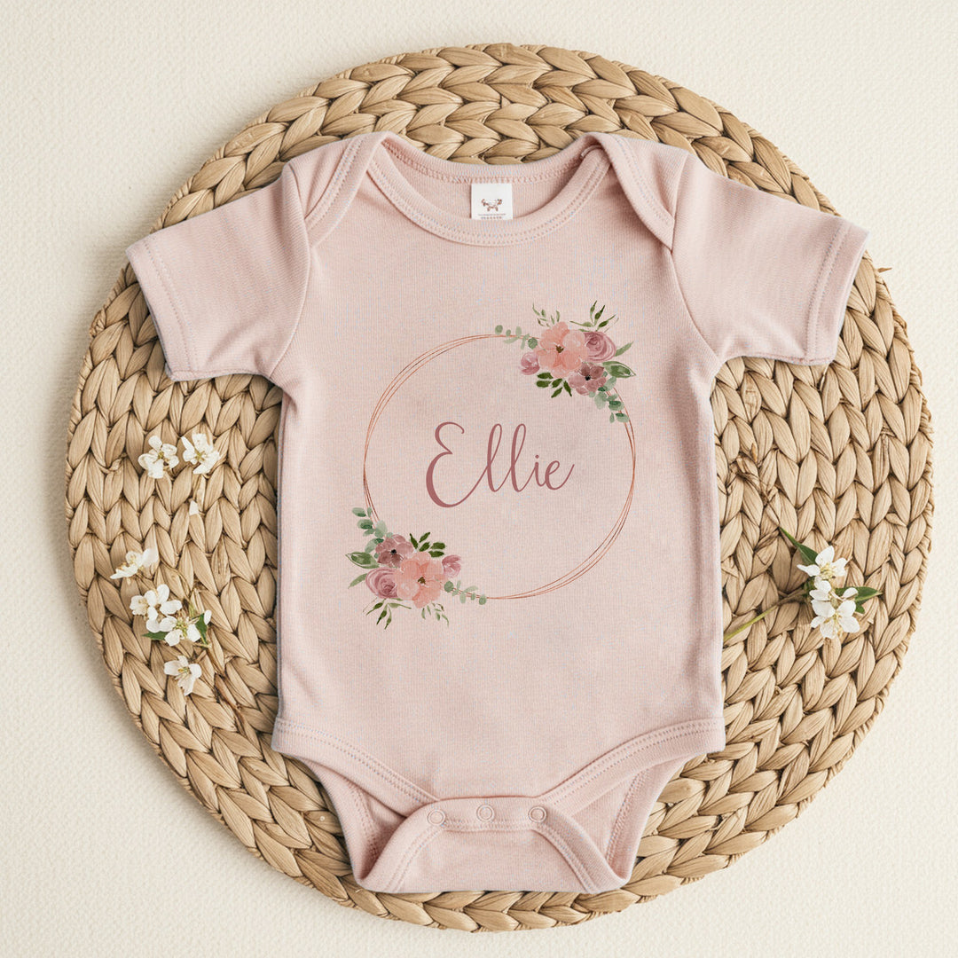 a personalised pink baby vest that says 'Ellie'. This design that features a pink and gold floral wreath