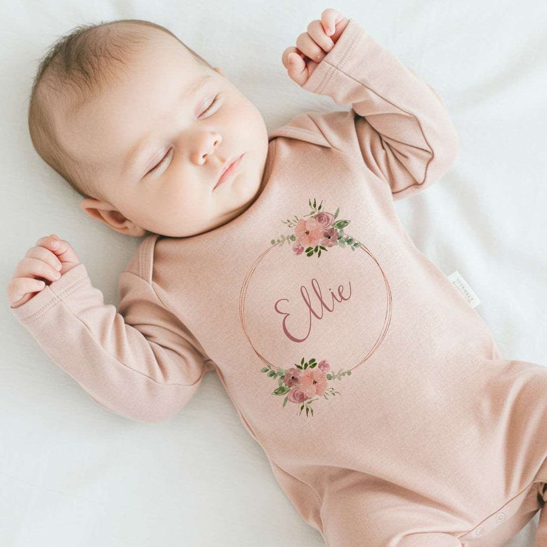 a personalised pink baby grow that says 'Ellie'. This design that features a pink and gold floral wreath