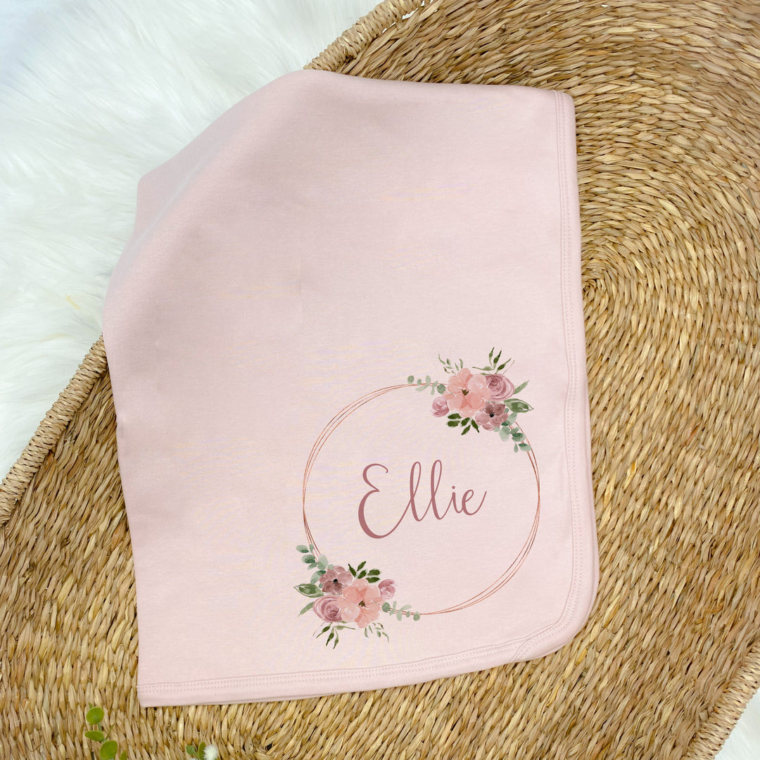 a personalised pink baby blanket that says 'Ellie'. This design that features a pink and gold floral wreath