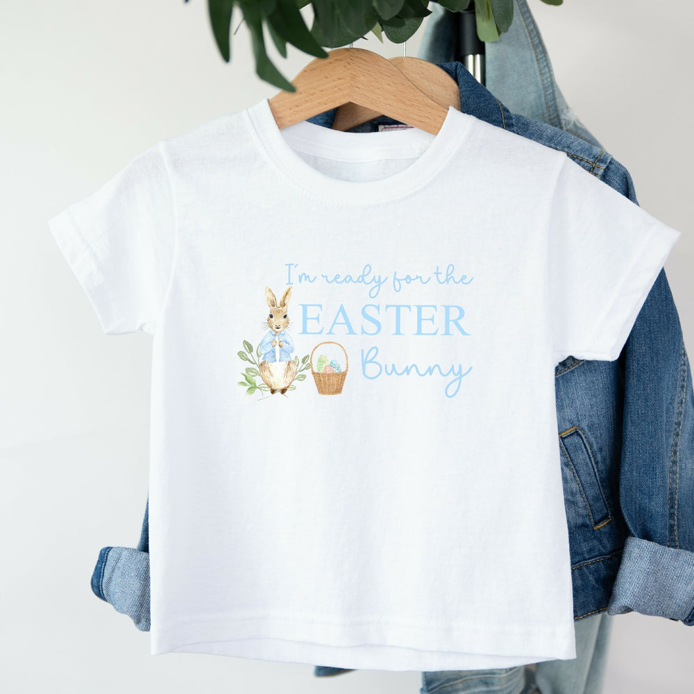 White childrens Easter t-shirt that says 'I'm ready for the Easter Bunny'. This design features a rabbit wearing a blue jacket standing next to an Easter basket full of eggs