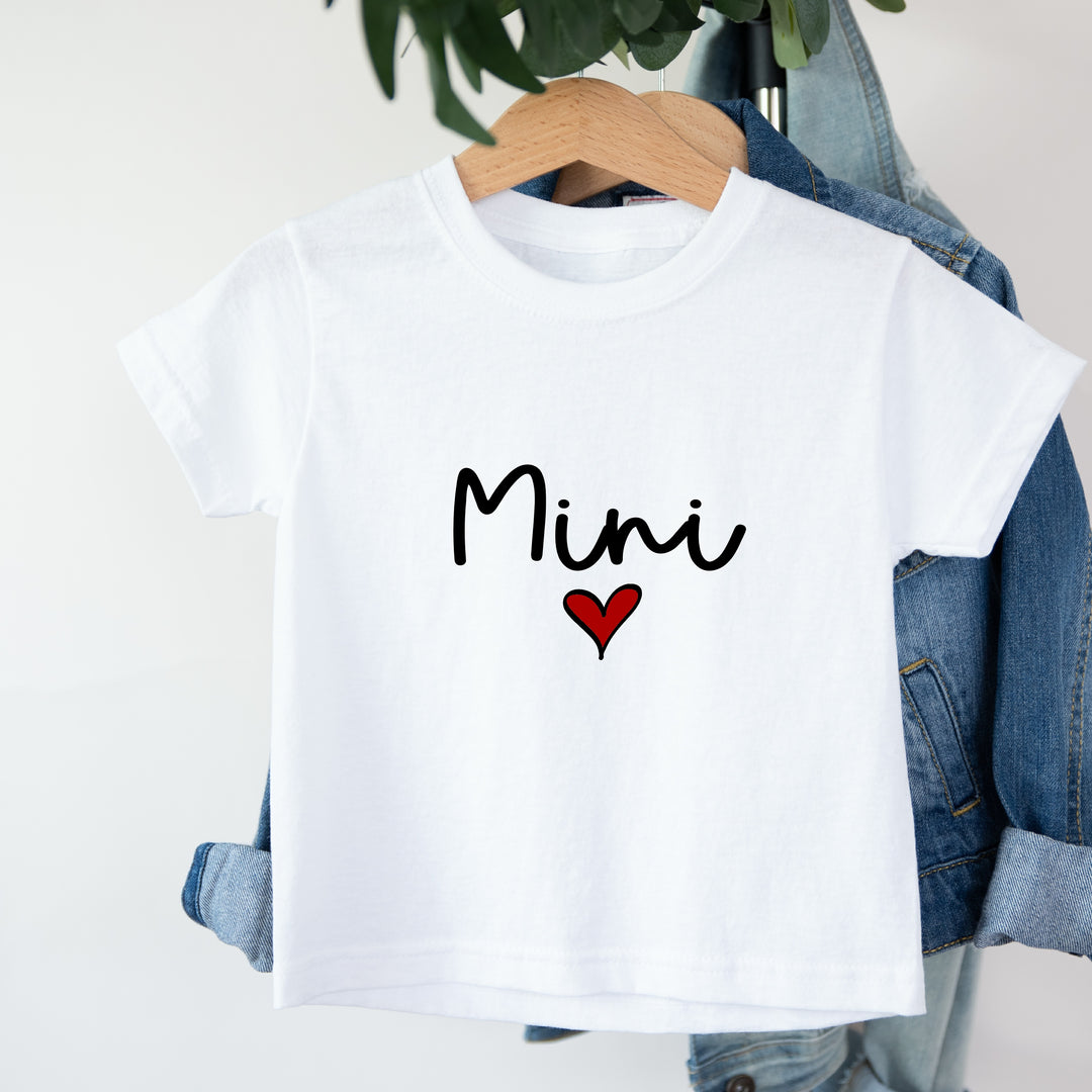 White t-shirt with 'Mini' and a heart on a hanger with jeans in the background