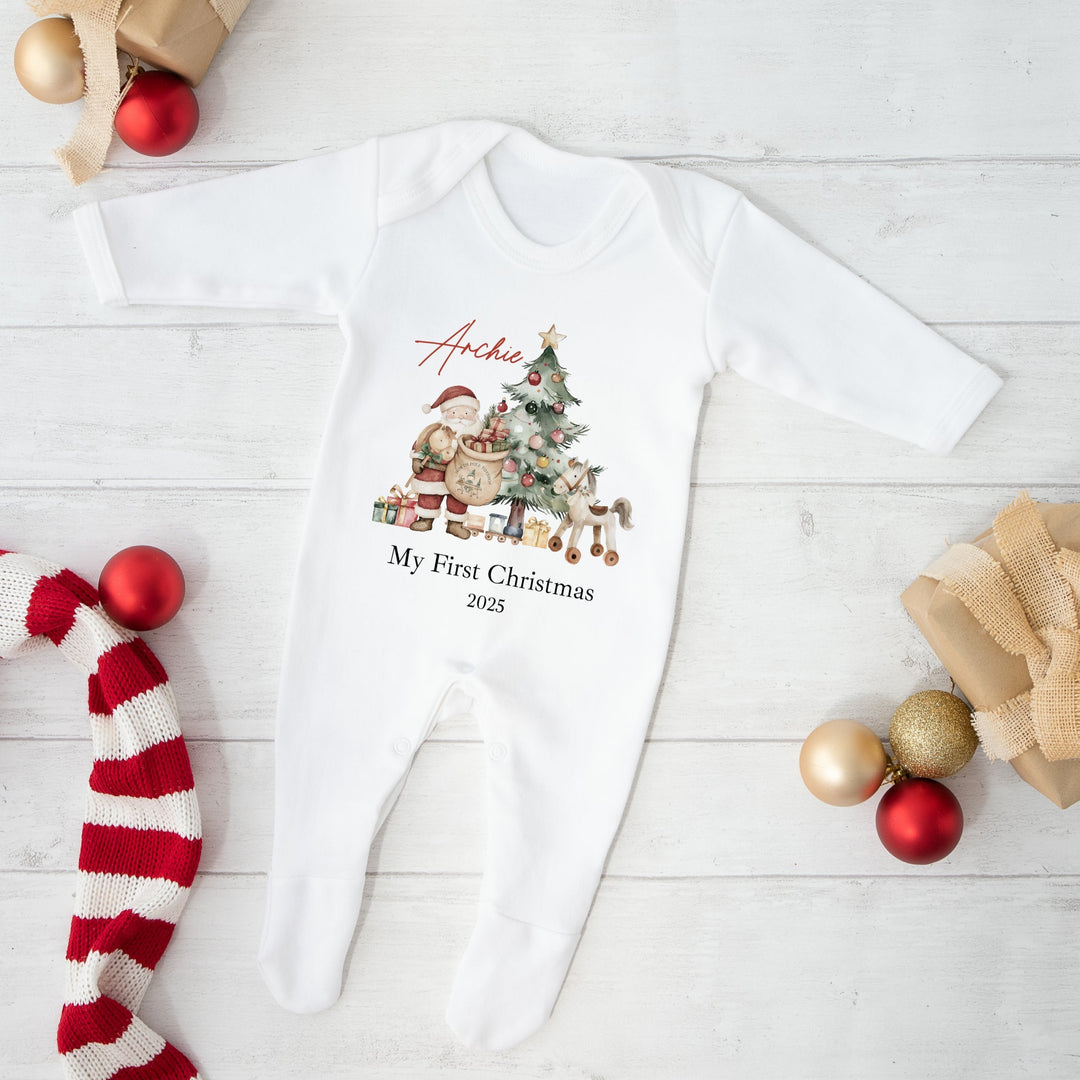 Baby onesie with Christmas design and text on a white wooden surface with festive decorations.