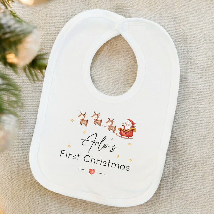 Baby bib with 'Arlo's First Christmas' text and Santa Claus design on a neutral background.