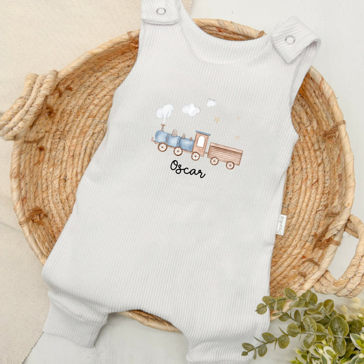 Personalised white ribbed dungarees that say 'Oscar'. This design features a blue train