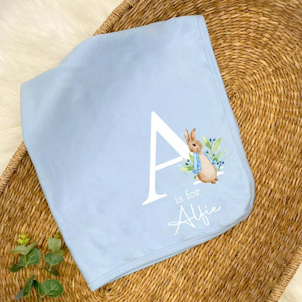 a personalised blue baby blanket that says 'A is for Alfie'. This design features a rabbit wearing a blue jacket