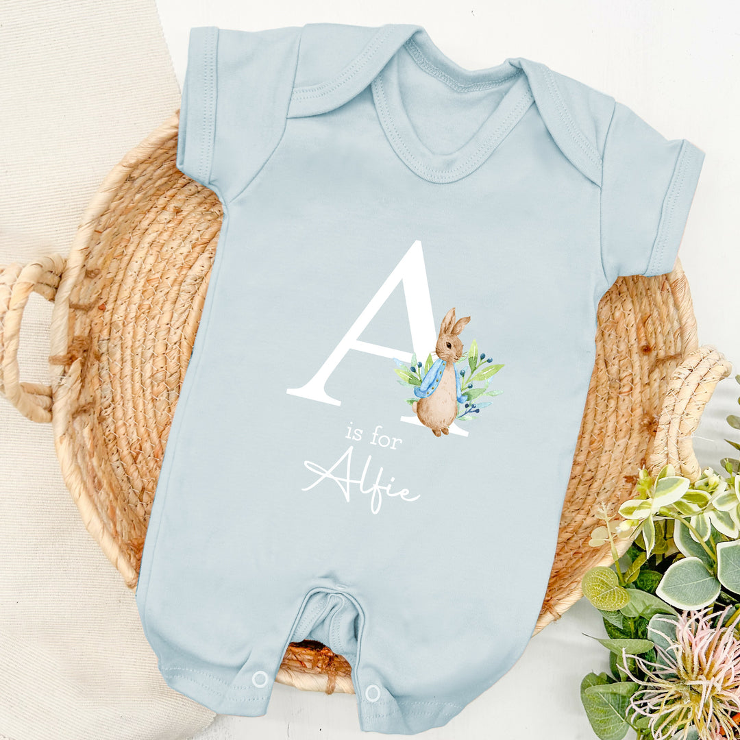 a personalised blue baby romper that says 'A is for Alfie'. This design features a rabbit wearing a blue jacket