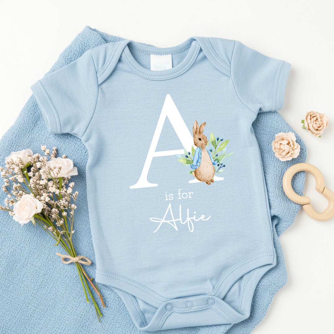 a personalised blue baby vest that says 'A is for Alfie'. This design features a rabbit wearing a blue jacket
