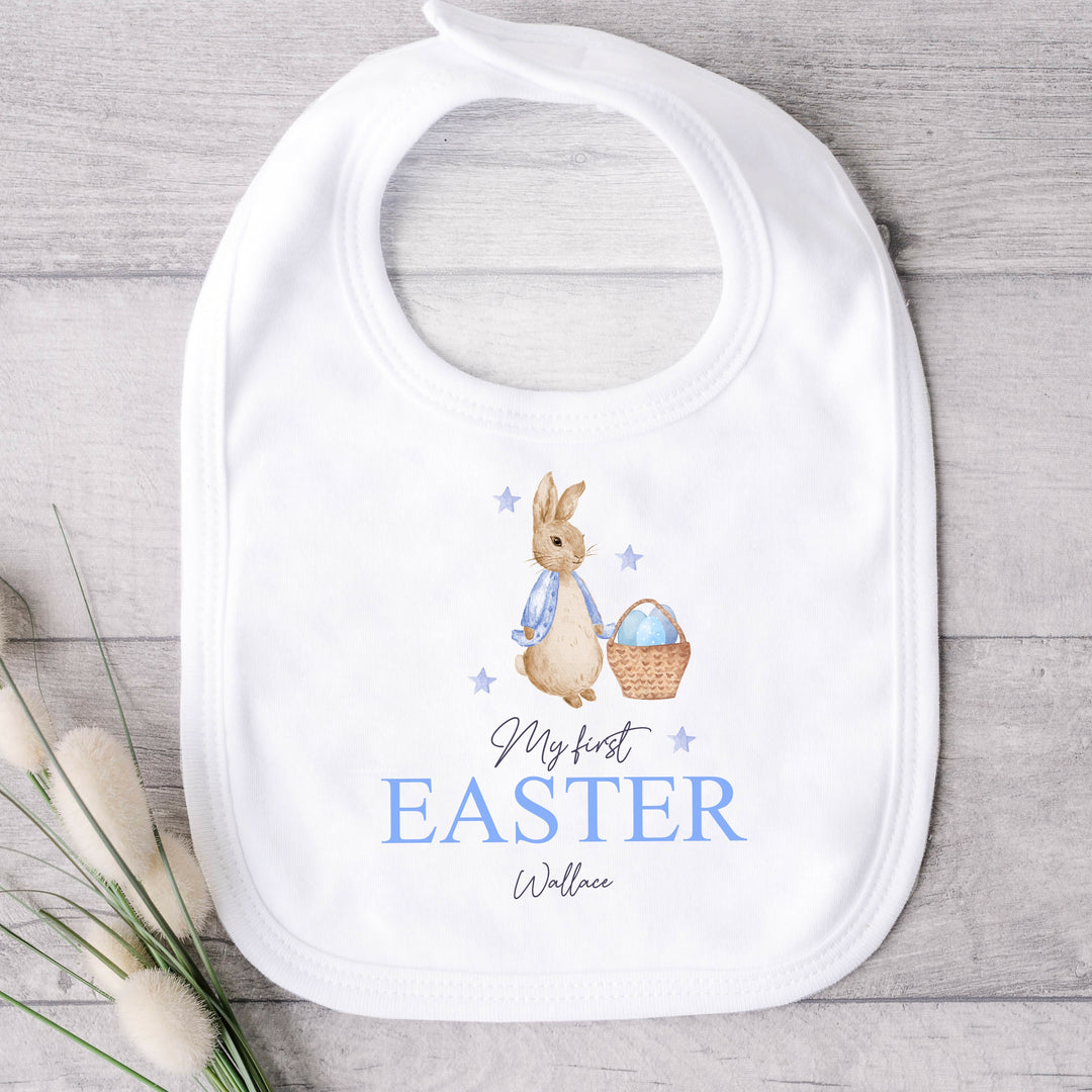 Personalised white Easter baby bib that says 'My First Easter Wallace'. This design features a rabbit with a blue jacket holding an Easter basket with blue stars around it