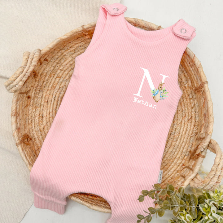 Personalised pink ribbed dungarees that say 'Nathan'. This design features a rabbit wearing a blue jacket