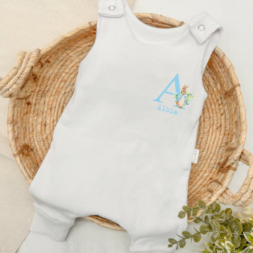 Personalised white ribbed dungarees that say 'Albie'. This design features a rabbit wearing a blue jacket