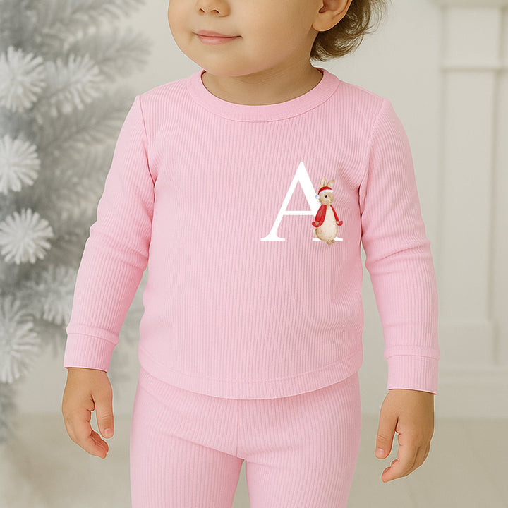 Child wearing pink pajamas with a letter 'A' and penguin design, standing in a festive room.