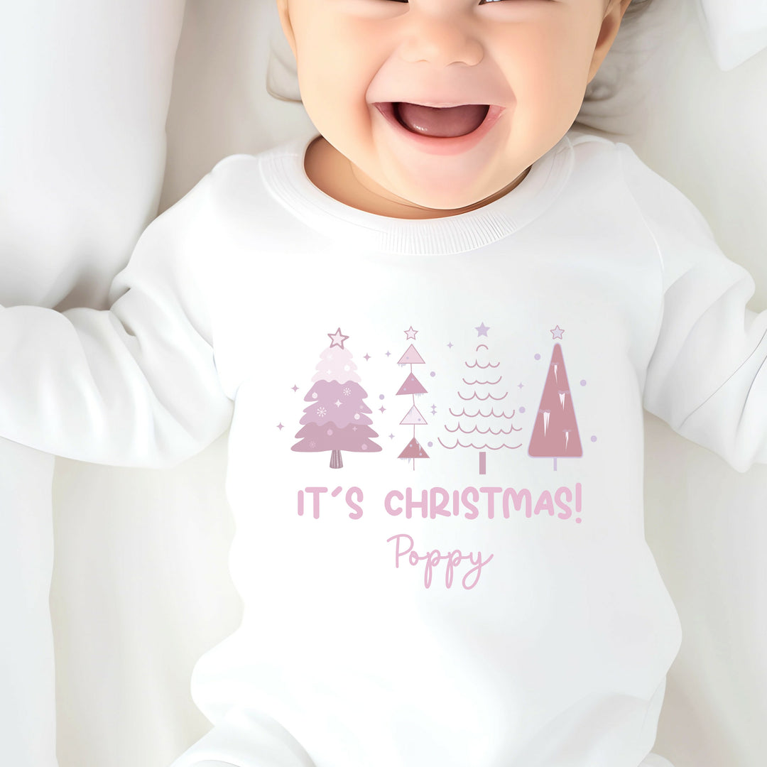 A white bodysuit with a personalized text and Christmas tree design, worn by a baby.