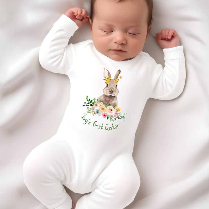 Personalised white Easter baby grow/sleepsuit that says 'Ivy's first Easter'. This design features a brown bunny in a floral wreath