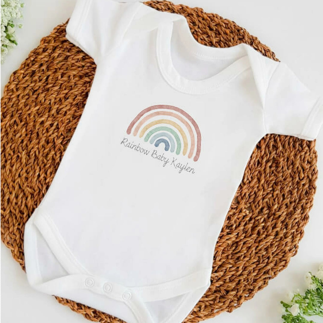 Baby announcement vests that says: Rainbow Baby Kaylen with a water colour rainbow above 