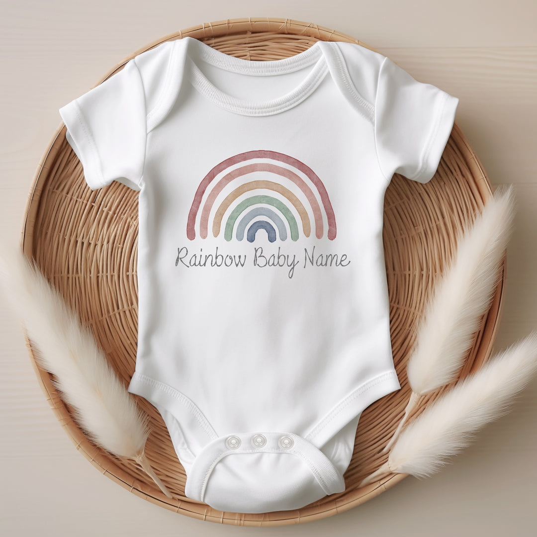 Baby announcement vests that says: Rainbow Baby Name with a water colour rainbow above 