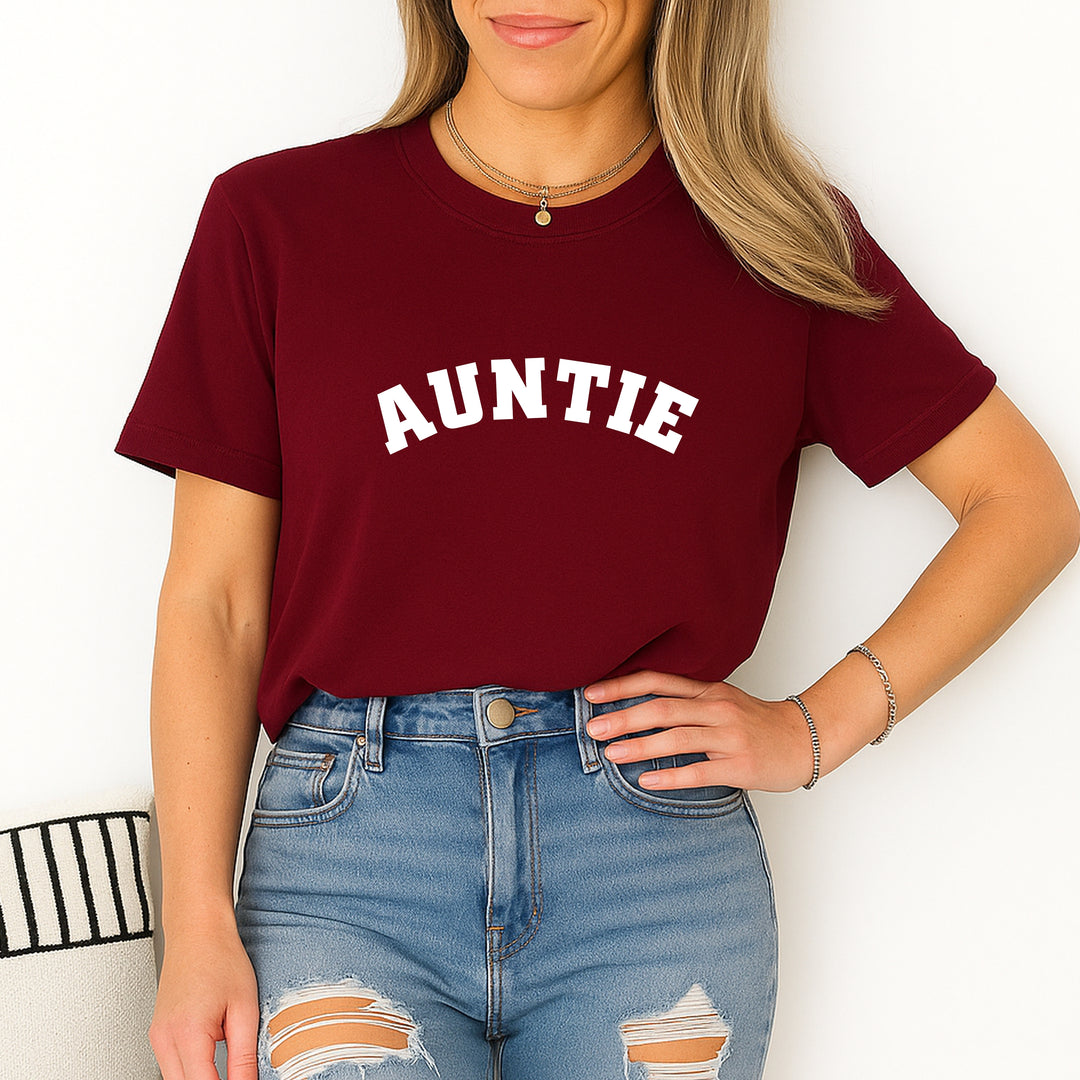 Person wearing a maroon t-shirt with 'AUNTIE' printed on it against a white background