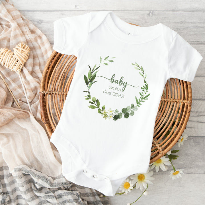 Baby announcement vests that says: baby Smith due 2023 with a green wreath around it 