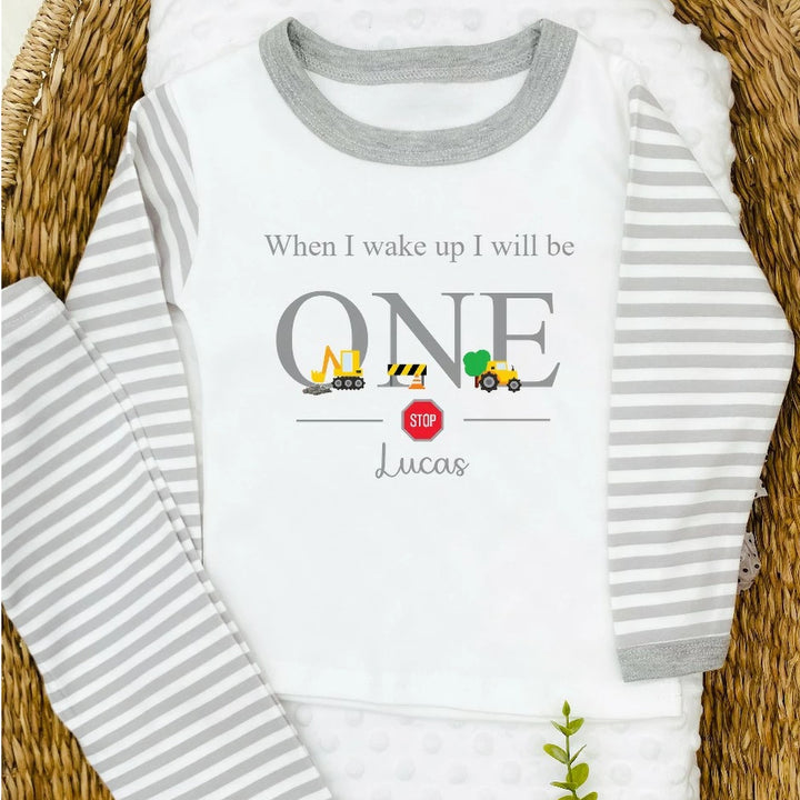 A pair of grey and white stripe children's birthday pyjamas with a grey digger design saying "When I wake up I will be One" with the name "Lucas".