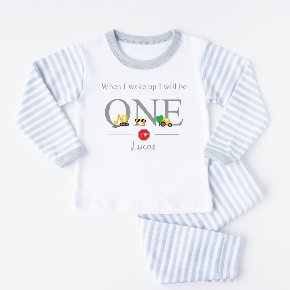 A pair of grey and white stripe children's birthday pyjamas with a grey digger design saying "When I wake up I will be One" with the name "Lucas".