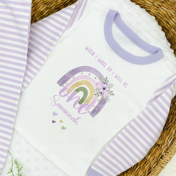 A pair of lilac and white stripe children's birthday pyjamas with a purple floral rainbow design saying "When I wake up I will be one" with the name "Savannah".