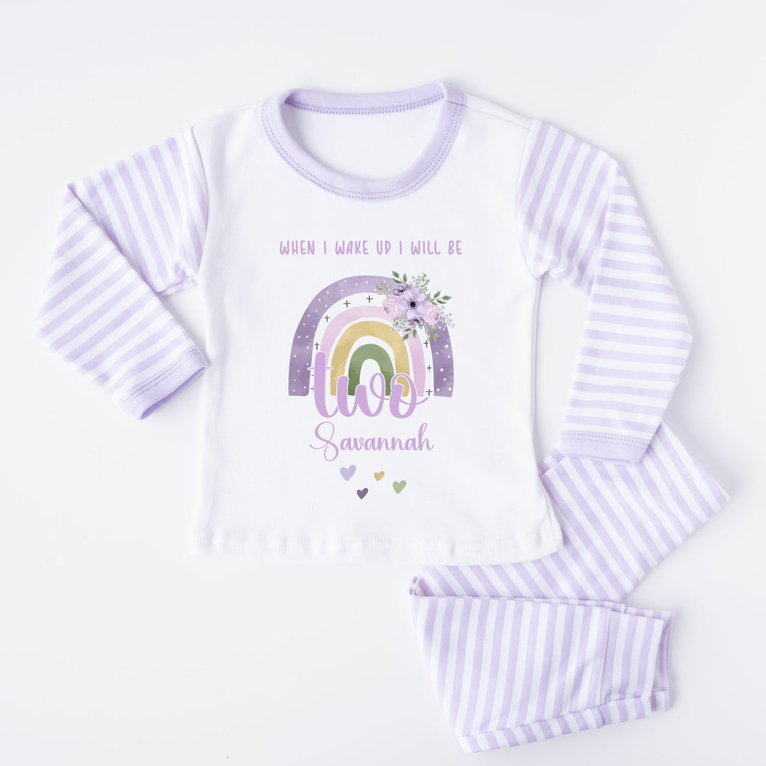 A pair of lilac and white stripe children's birthday pyjamas with a purple floral rainbow design saying "When I wake up I will be two" with the name "Savannah".