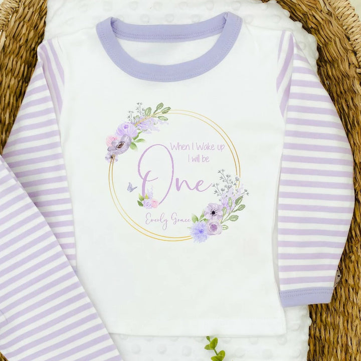 A pair of lilac and white stripe children's birthday pyjamas with a purple floral butterfly wreath design saying "When I wake up I will be One" with the name "Everly Grace".