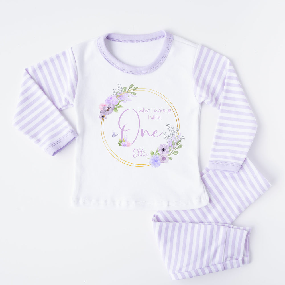 A pair of lilac and white stripe children's birthday pyjamas with a purple floral butterfly wreath design saying "When I wake up I will be One" with the name "Ellie".