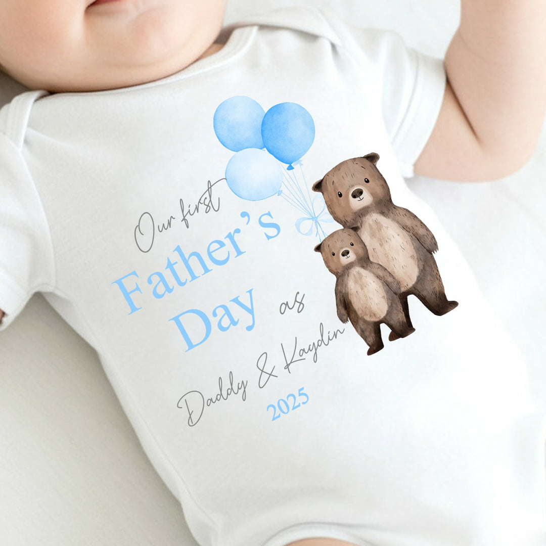 Personalised white Father's Day baby vest that says 'Our First Father's Day as Daddy & Kaydin 2025'. This design features 2 brown bears holding 3 blue balloons