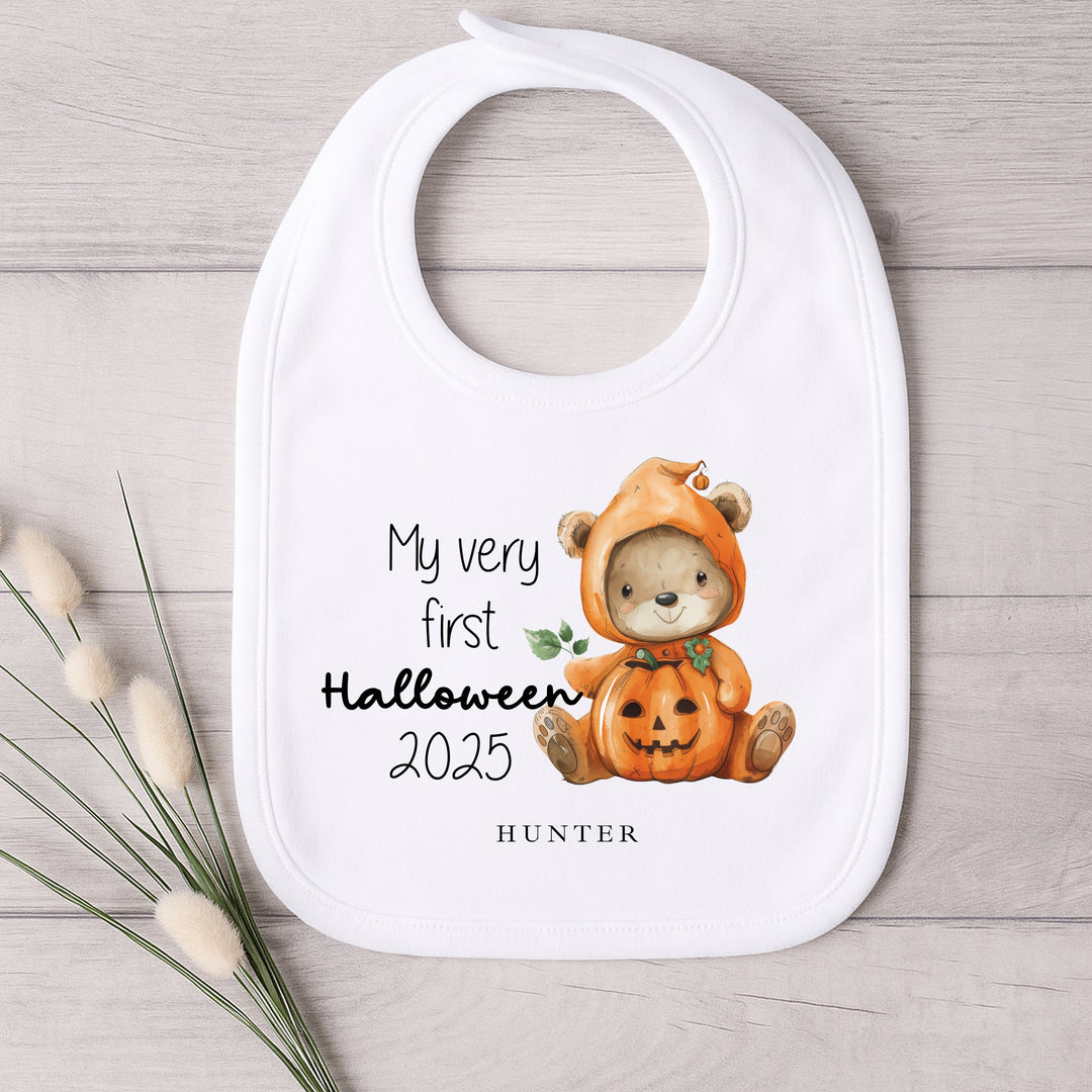 Baby bib with a bear in a pumpkin costume for Halloween 2025 on a wooden surface.