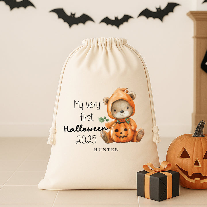 Drawstring bag with a bear in a pumpkin costume and 'My very first Halloween 2025' text, next to a small gift box and pumpkin.