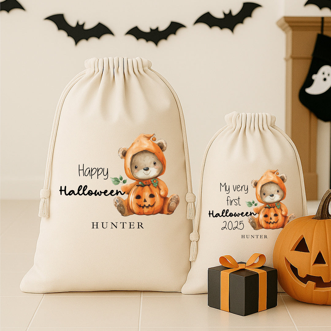 Two Halloween-themed drawstring bags with a bear in a pumpkin costume, pumpkins, and gift box on a neutral background.
