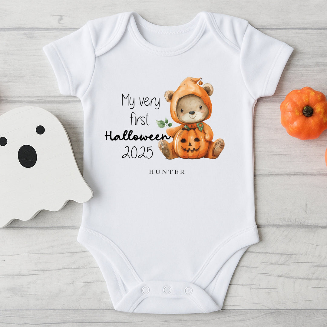 Baby onesie with Halloween design and text on a wooden surface with decorative items.