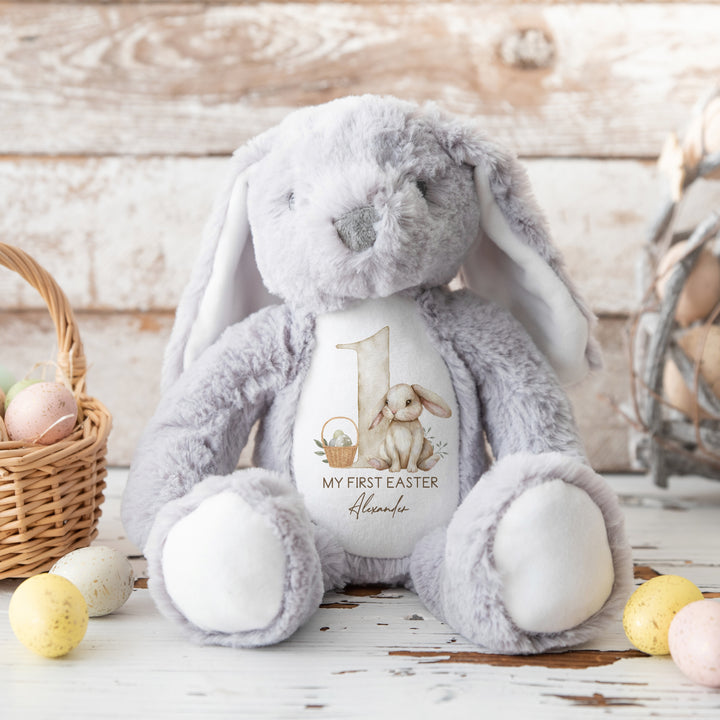 A personalised grey Easter Teddy that says 'My First Easter Alexander'. This design features a big beige 1 with a beige rabbit and Easter basket next to it.