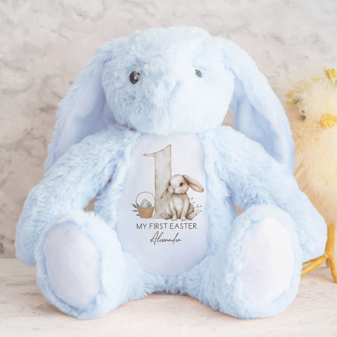 A personalised blue Easter Teddy that says 'My First Easter Alexander'. This design features a big beige 1 with a beige rabbit and Easter basket next to it.