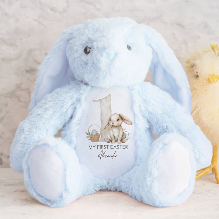 A personalised blue Easter Teddy that says 'My First Easter Alexander'. This design features a big beige 1 with a beige rabbit and Easter basket next to it.