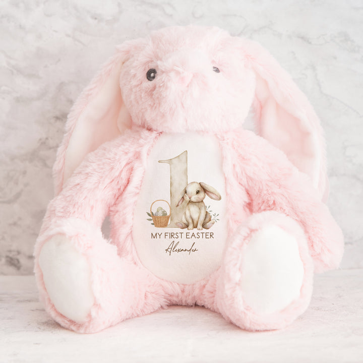 A personalised pink Easter Teddy that says 'My First Easter Alexander'. This design features a big beige 1 with a beige rabbit and Easter basket next to it.