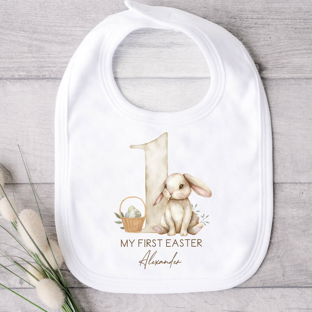 Personalised white Easter bib that says 'My First Easter Alexander'. This design features a big beige 1 and a brown rabbit and an Easter basket