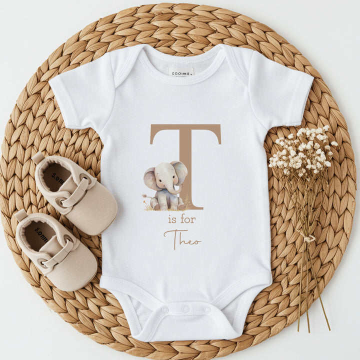A personalised white baby bib that says 'A is for Alexa' in beige text. This design features an elephant sitting next to a big beige A