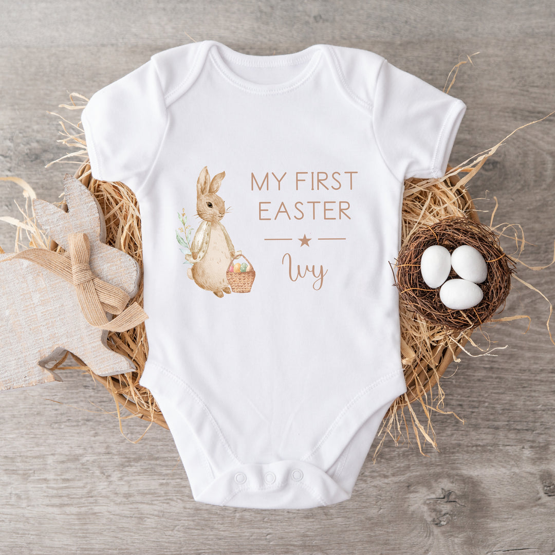 Personalised white Easter baby vest that says 'My First Easter Ivy'. This design features a rabbit wearing a beige jacket 