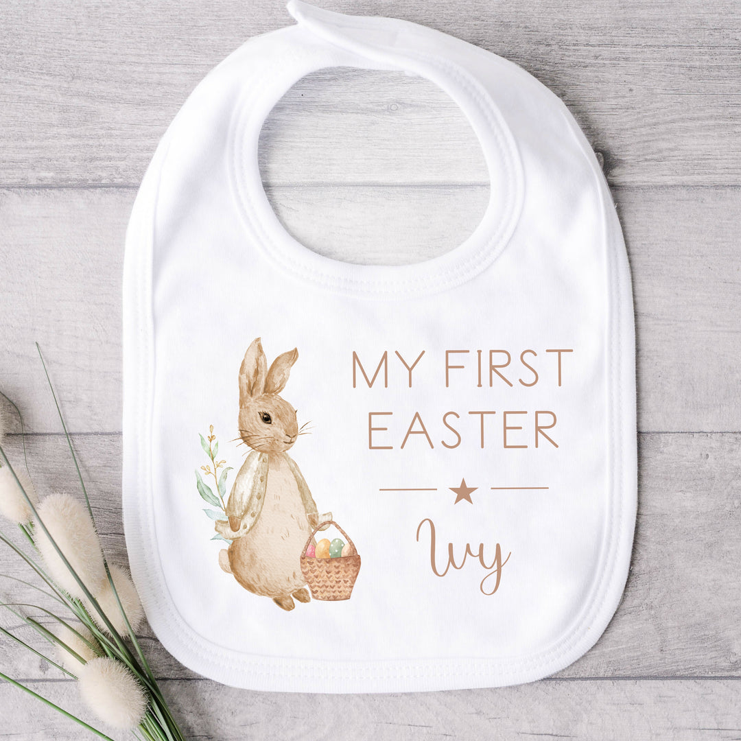 Personalised white Easter baby bib that says 'My First Easter Ivy'. This design features a rabbit wearing a beige jacket 