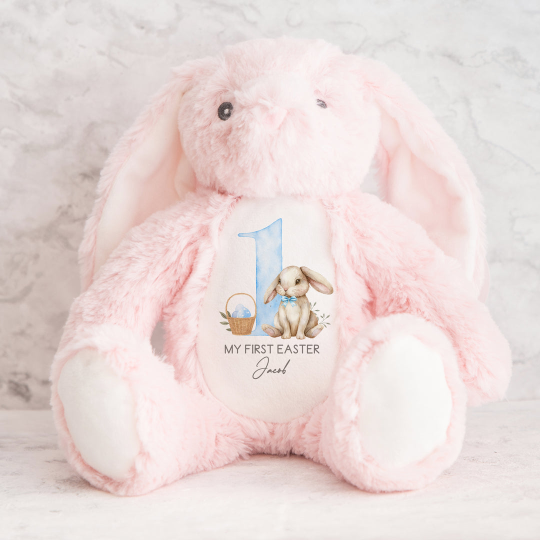 Personalised pink bunny Easter teddy that says 'My First Easter Jacob'. This design features a big blue 1 with a bunny sitting next to it wearing a blue bow tie and an Easter basket