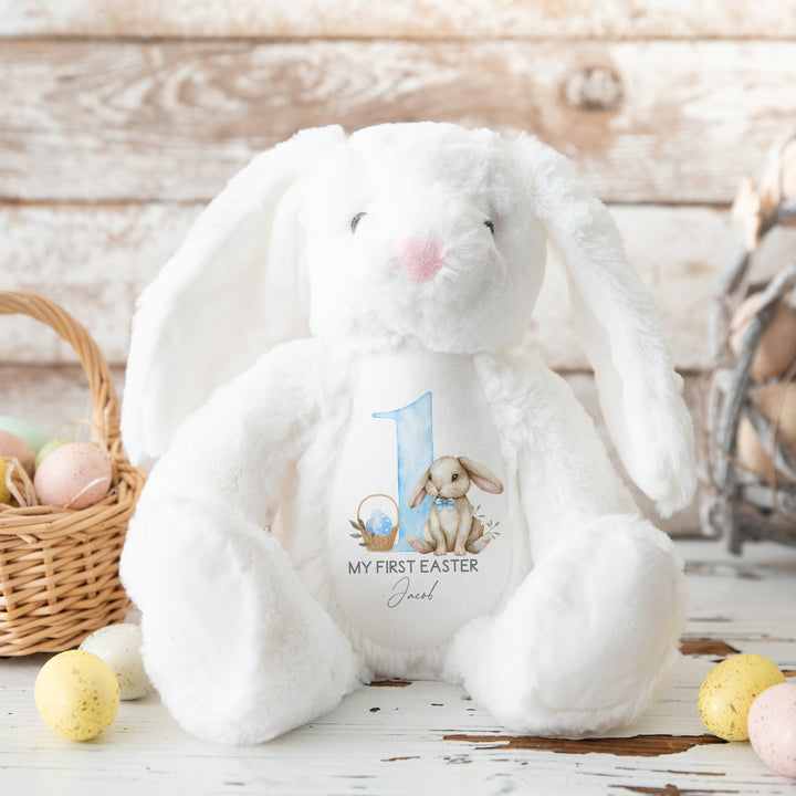 Personalised white bunny Easter teddy that says 'My First Easter Jacob'. This design features a big blue 1 with a bunny sitting next to it wearing a blue bow tie and an Easter basket