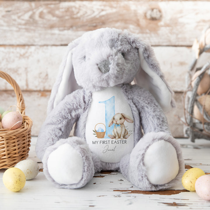 Personalised grey bunny Easter teddy that says 'My First Easter Jacob'. This design features a big blue 1 with a bunny sitting next to it wearing a blue bow tie and an Easter basket