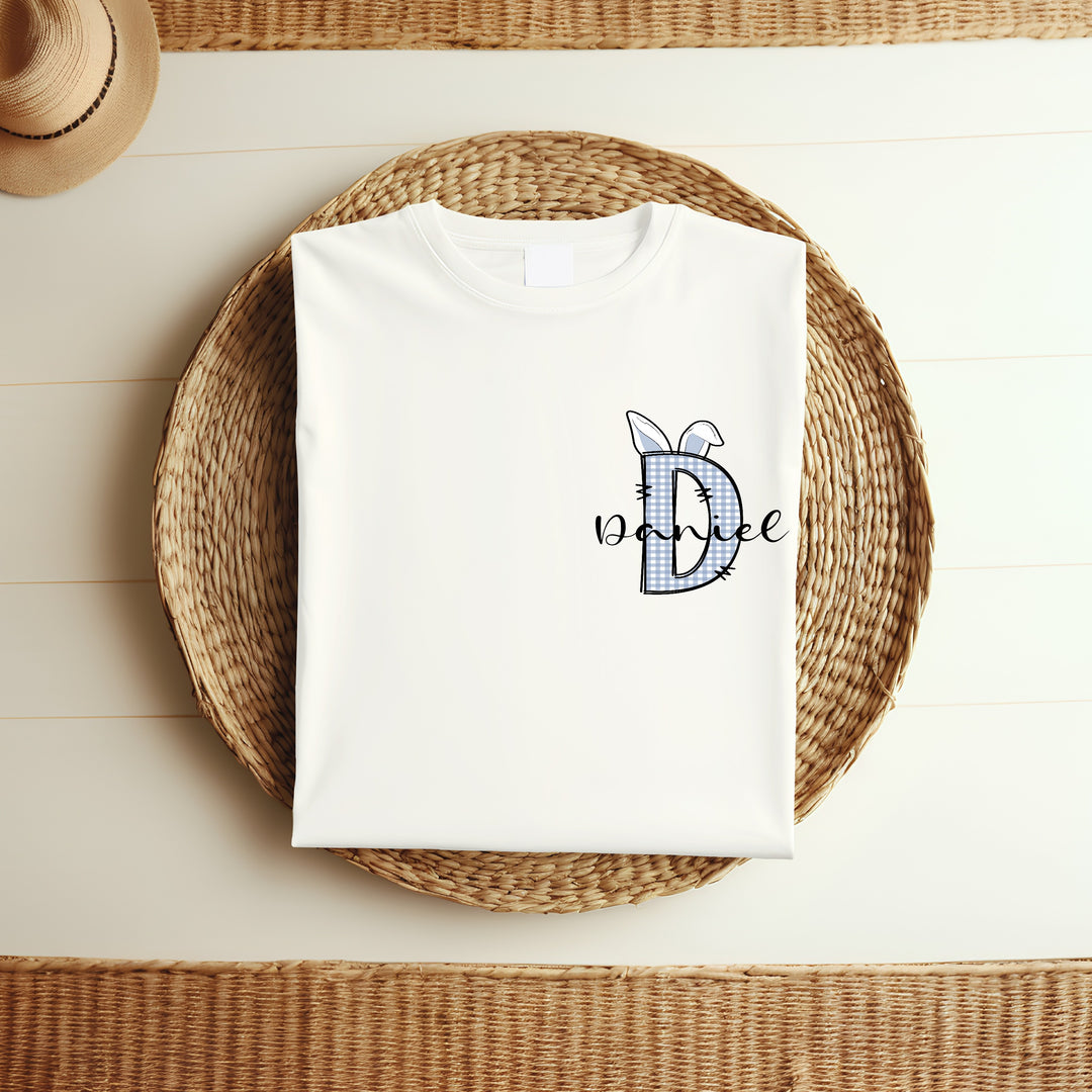 Personalised white Easter t-shirt that says 'D Daniel'. This design features a blue tartan D with blue bunny ears on it 