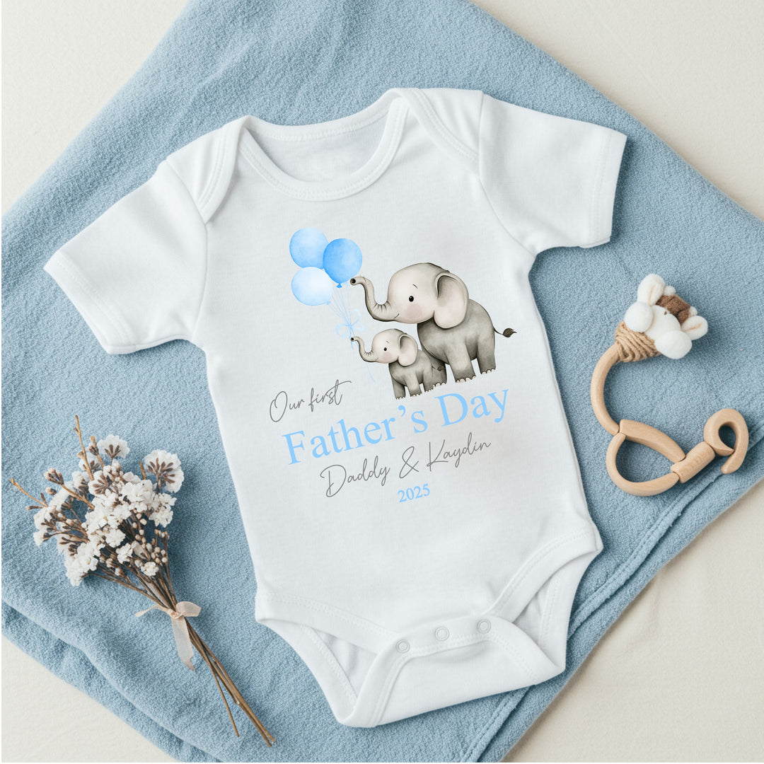 Personalised white Father's Day baby vest that says 'Our First Father's Day Daddy & Kaydin 2025'. This design features 2 grey elephants holding 3 blue balloons