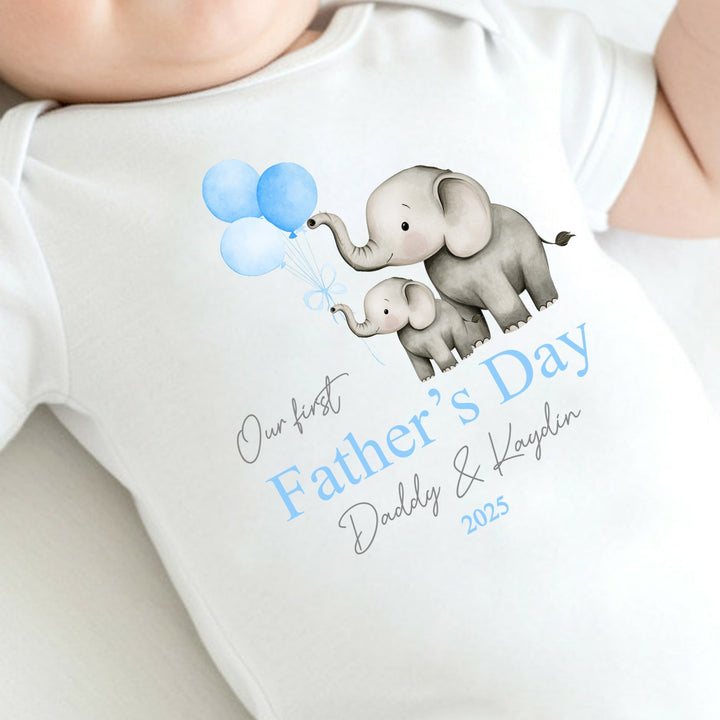 Personalised white Father's Day baby vest that says 'Our First Father's Day Daddy & Kaydin 2025'. This design features 2 grey elephants holding 3 blue balloons